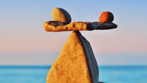 Rocks balancing on a rock like a see-saw in front of an expanse of water